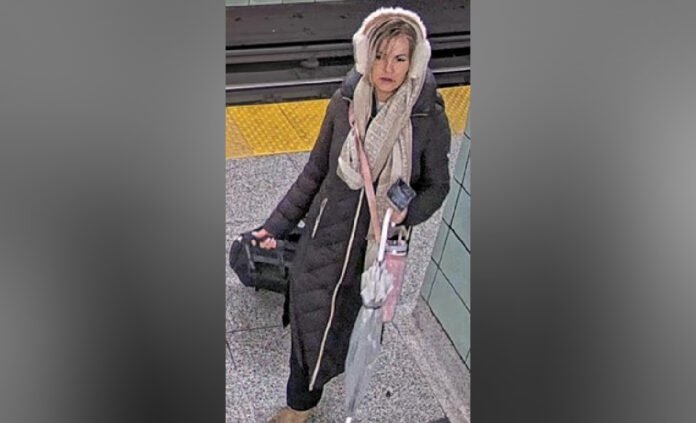 Security camera image of a woman wanted in a suspected hate-motivated mischief investigation. She is wearing earmuffs, a long black coat, a light-coloured scarf, and brown boots while walking through a TTC station.