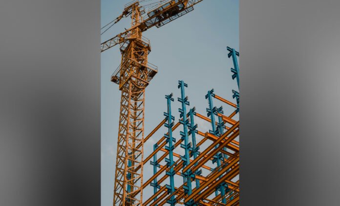 A construction site showing a tall tower crane beside a partially built framework