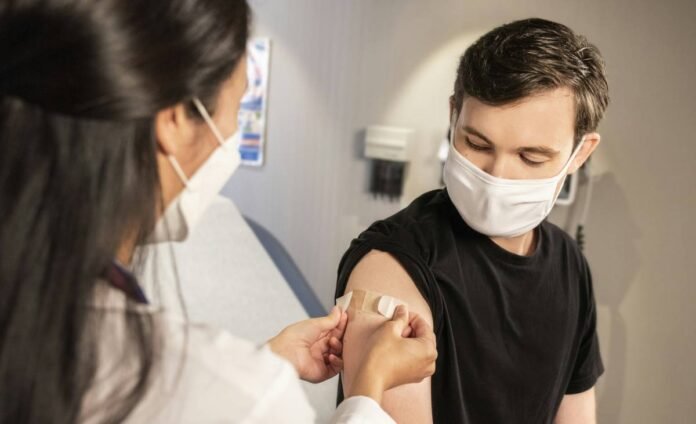 Helathcare worker administer a vaccine injection into masked patient's upper arm inside a clinic