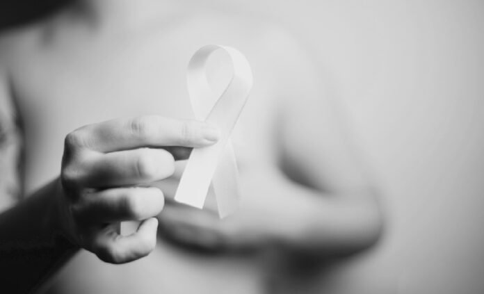 A hand gently holding a white awareness ribbon against a softly blurred background, symbolizing cancer awareness and support.