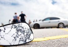 Fatal crash in Markham leaves one dead, another seriously injured Cracked and shattered car side mirror in the foreground after a collision, with a damaged white vehicle stopped on the roadside and several people standing nearby as police investigate.