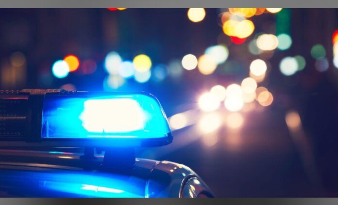 Close-up of flashing blue emergency lights with blurred, colorful city lights glowing in the background at night.