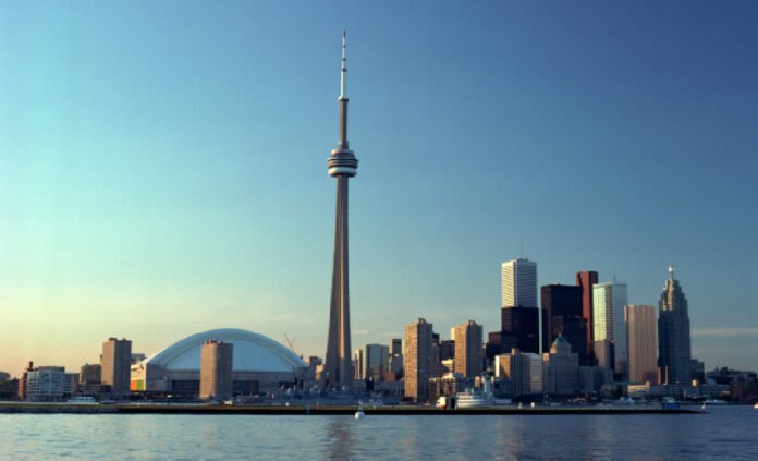 A wide view of Toronto's waterfront skyline at sunset, with CN Tower and surrounded by downtown highrise buildings