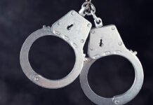 Halton Police arrested two suspects in Oakville dealership break-In Silver metal handcuffs with keys attached, shown against a dark background.