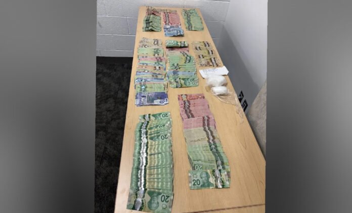 A table displaying seized evidence, including multiple stacks of Canadian currency in various denominations arranged in rows, alongside several small plastic bags containing a white powder believed to be drugs, photographed as part of a police seizure.