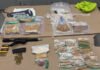 Man and woman charged After firearm and fentanyl seizure in Toronto Photo shows police-seized evidence laid out on a table, including a rifle with magazine, boxes of ammunition, and numerous plastic bags containing suspected fentanyl for documentation.