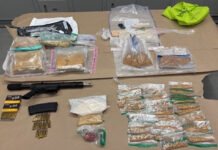 Man and woman charged After firearm and fentanyl seizure in Toronto Photo shows police-seized evidence laid out on a table, including a rifle with magazine, boxes of ammunition, and numerous plastic bags containing suspected fentanyl for documentation.