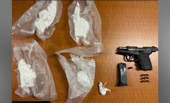 A photo of evidence laid out on a wooden table, including a black semi-automatic handgun, a detached magazine, several loose bullets, and multiple clear plastic bags containing a white powdery substance.
