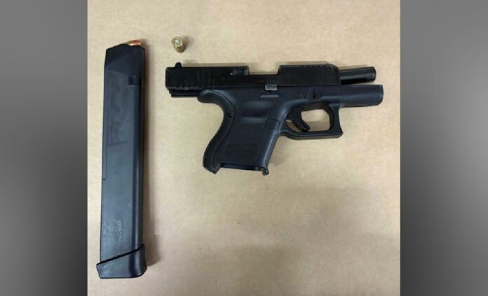 A black handgun on a light surface with a separate extended magazine placed beside it.