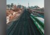 Metrolinx CEO apologizes to GO train riders for delays since train derailment A green-and-white commuter train travels along elevated railway tracks, with the tracks converging into the distance. In the background, Toronto’s skyline is visible, including the CN Tower, under an overcast sky.