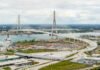 Democrats say they’re escalating investigation into Gordie Howe bridge debacle Aerial view of a large cable-stayed bridge under construction spanning a river, with curved access roads and construction activity on both sides.