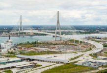 Democrats say they’re escalating investigation into Gordie Howe bridge debacle Aerial view of a large cable-stayed bridge under construction spanning a river, with curved access roads and construction activity on both sides.