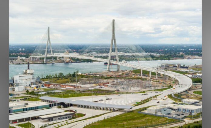Gordie Howe bridge Aerial view of a large cable-stayed bridge under construction spanning a river, with curved access roads and construction activity on both sides.