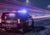 Transport truck slides into ditch, shuts down lanes on QEW toward Toronto ntario Provincial Police cruiser with flashing red and blue lights parked on the shoulder of a highway at night, as long-exposure light trails from passing traffic streak past the scene.