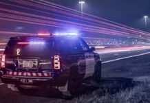 Transport truck slides into ditch, shuts down lanes on QEW toward Toronto ntario Provincial Police cruiser with flashing red and blue lights parked on the shoulder of a highway at night, as long-exposure light trails from passing traffic streak past the scene.