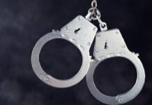 Three arrested, fourth wanted in Milton–Halton Hills copper wire theft investigation A close-up image of a pair of metal handcuffs with a short chain linking the two cuffs, shown against a dark background.