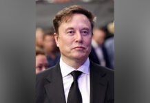 Ontario’s payout to Elon Musk over cancelled Starlink contract to remain secret image of Elon Musk wearing a black suit, white shirt, and black tie stands facing the camera with a neutral expression. The background is blurred with several people visible behind him, suggesting a public or formal event setting.