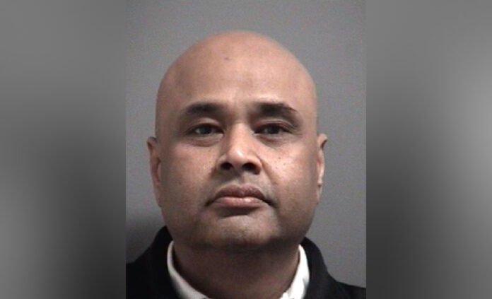 headshot photo of a middle-aged man facing the camera. He has a shaved head, a slight moustache and stubble, and is wearing a dark jacket.