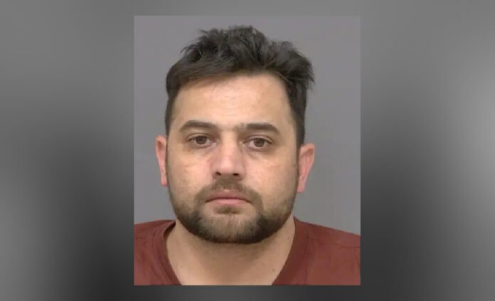 arrested_in_dangerous_driving Close-up of a man with short dark hair and a trimmed beard, looking straight at the camera with a neutral expression against a plain background.