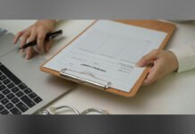 Ontario surpasses primary care goals ,rolls out provoncewide EMR system Hands holding a clipboard with a patient chart while another hand uses a pen next to a laptop and stethoscope on a desk.